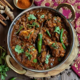 Lahori Chicken Karahi in a traditional karahi, garnished with green chilies, ginger, and cilantro, surrounded by whole spices on a rustic wooden surface.