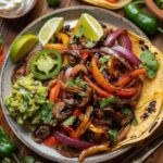 Colorful Veggie Fajitas with bell peppers, onions, and mushrooms, garnished with cilantro and lime wedges, served with tortillas, guacamole, and pico de gallo on a rustic wooden table.